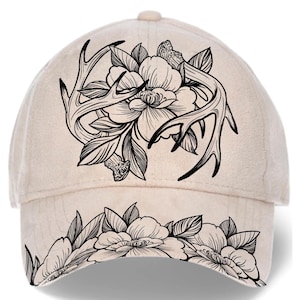 May include: A beige baseball cap featuring a black floral and antler design. The cap has a curved brim with a floral pattern and a button on top. The design includes detailed flowers and leaves.