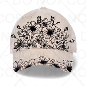 May include: A cream-coloured baseball cap with a black floral design. The design features detailed outlines of flowers and leaves across the front and brim. The cap has a curved peak and a rounded crown.