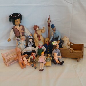 May include: A collection of vintage wooden dolls, including a family of five, a baby in a crib, and a doll holding a paint palette. The dolls are dressed in various colorful outfits and have painted faces.