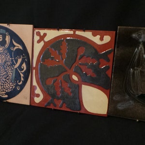 May include: Three ceramic tiles with different designs. The first tile features a black and white illustration of a person playing a musical instrument. The second tile has a black and white illustration of a stylized leaf. The third tile has a black and white illustration of a bird in flight.