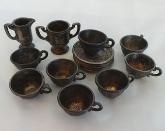 May include: A set of miniature silver-toned teacups and saucers, a creamer, and two small cups with handles. The set is arranged on a white surface.