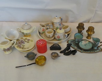May include: A miniature tea set with a teapot, creamer, sugar bowl, cups, saucers, and a tray. There are also two small lamps, a purse, a red box, and two pairs of shoes.