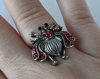 May include: A silver ring with a red jeweled beetle design.