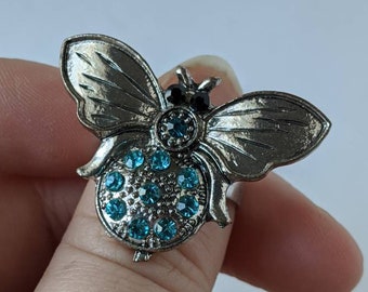 May include: A silver ring with a butterfly design. The butterfly has blue rhinestones on its body and black rhinestones for eyes.
