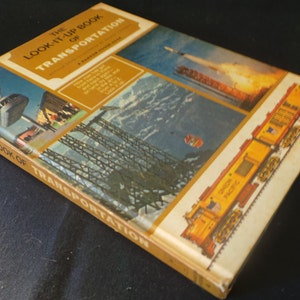 May include: The Look-It-Up Book of Transportation, a vintage book with a yellow cover and colorful images of different modes of transportation, including a monorail, a rocket, a bridge, and a train.