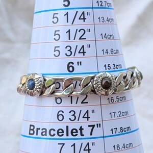 May include: Silver-toned chain bracelet with decorative circular accents. The bracelet is measured on a sizing cone, appearing to be approximately 6 inches (15.3 cm) in diameter. The bracelet has a classic curb chain design.