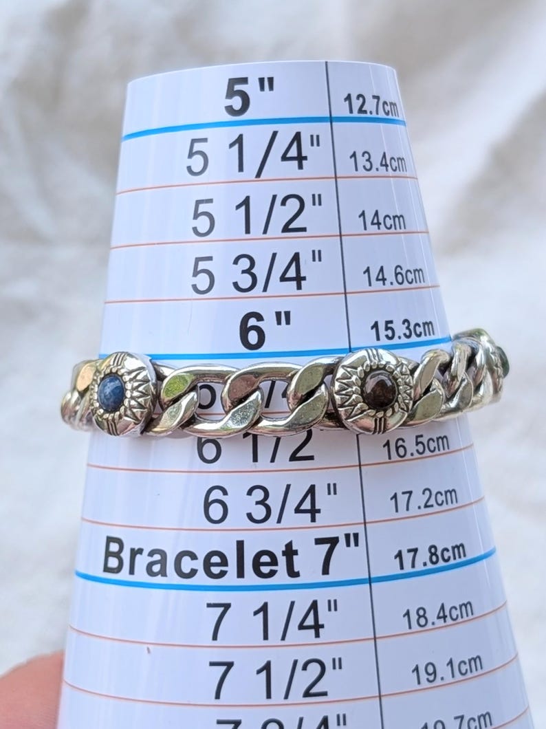 May include: Silver-toned chain bracelet with decorative circular accents. The bracelet is measured on a sizing cone, appearing to be approximately 6 inches (15.3 cm) in diameter. The bracelet has a classic curb chain design.