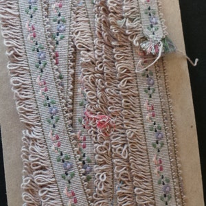 Puede incluir: Primer plano de una cinta beige con un patr&oacute;n floral y un borde de flecos. La cinta est&aacute; hecha de tejido tejido y tiene un aspecto delicado y femenino.