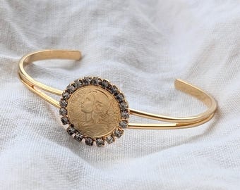 Pulsera tipo brazalete vintage de tono dorado con moneda francesa de 1987 y diamantes de imitación.