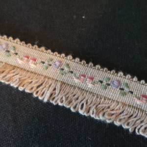 Puede incluir: Un ribete beige con flecos y un patr&oacute;n floral en tonos de rosa, morado, verde y negro.