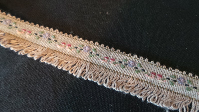 Puede incluir: Un ribete beige con flecos y un patr&oacute;n floral en tonos de rosa, morado, verde y negro.