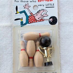 May include: Vintage miniature bowling set in a clear plastic package. The set includes wooden bowling pins with red stripes, a black bowling ball, and a gold trophy. The packaging features a cartoon illustration and the text "For those who BOWL very LITTLE."