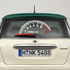 Op de afbeelding: Een witte Mini Cooper met een groen dak. De auto heeft een kentekenplaat met de tekst "M NK 5488". De achterruit heeft een sticker van een snelheidsmeter met een rode naald.