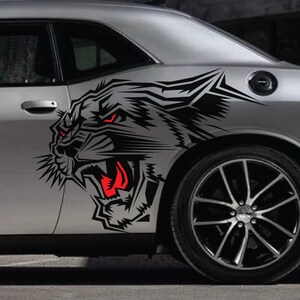 May include: A black and white graphic of a snarling panther with red eyes is printed on the side of a silver car. The panther graphic is a car decal.