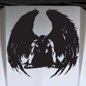 May include: Black and white silhouette of an angel with large wings, kneeling with its head bowed. The angel is depicted in a distressed, grunge style.
