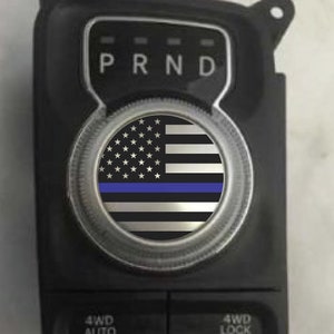 May include: A black and silver car gear shift knob with a thin blue line American flag decal. The decal features white stars on a blue field and red and white stripes.