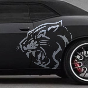 Puede incluir: Un coche negro con una calcomanía de pantera gris en el lateral. La pantera está mirando hacia adelante con la boca abierta y los dientes visibles.