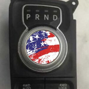 May include: A black car gear shift knob with a distressed American flag design. The knob has the letters "PRND" printed on it.