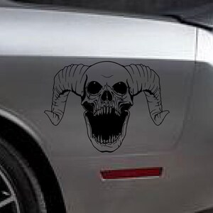 May include: Black and white decal of a skull with horns. The skull has a wide open mouth with sharp teeth. The decal is on a grey car.