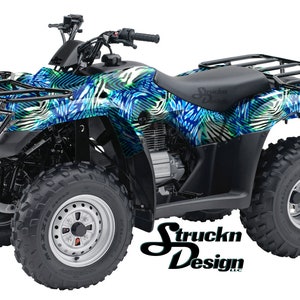 May include: A blue and green patterned ATV with black wheels and a black metal rack on the back. The ATV is on a white background.