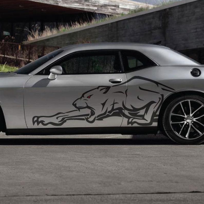 Op de afbeelding: Een zilveren auto met een zwarte panter sticker aan de zijkant. De panter is in een rennende pose met zijn bek open en zijn ogen gloeien rood.