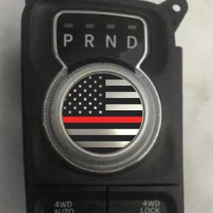 May include: A black and silver car gear shift knob with a thin red line across the centre of an American flag design.