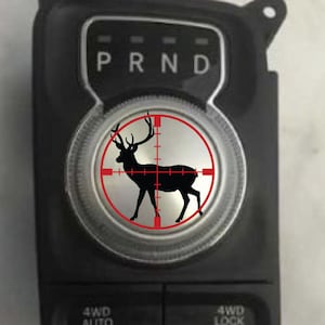 May include: A black and white deer silhouette inside a red target circle on a black and silver gear shift knob. The gear shift knob has the letters "PRND" printed on it.