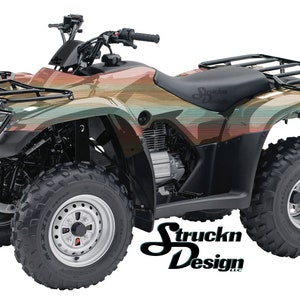 May include: A black ATV with a wood-grain patterned design in shades of brown, green, and orange. The ATV has a black seat, a black roll cage, and black wheels with silver rims. The ATV is on a white background. The text "Struckn Design" is visible on the side of the ATV.