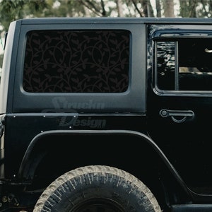 May include: Black Jeep Wrangler with a black floral design on the rear window. The Jeep has a spare tire on the back and a black door handle.