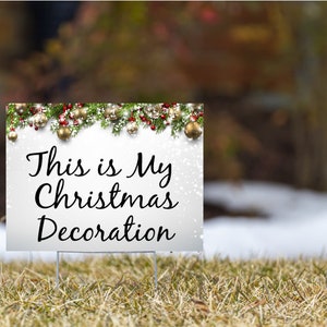 Puede incluir: Señal blanca con fondo nevado y una guirnalda verde con bayas rojas y adornos dorados en la parte superior. La señal dice "This is My Christmas Decoration".