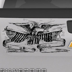 May include: A black and white graphic of an eagle with outstretched wings, holding a banner with the American flag design. The banner is draped across the eagle's chest. The image is a decal.