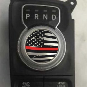 May include: A black and white American flag with a red stripe across the middle. The flag is on a round, silver-coloured knob with the letters "PRND" above it.