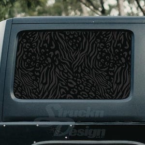 May include: Black and white zebra and leopard print car window decal. The decal is applied to the rear window of a black SUV.