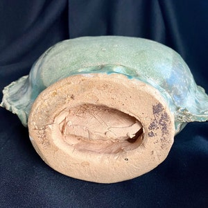 K&ouml;nnte beinhalten: Die Unterseite einer gr&uuml;n glasierten Keramikschale mit einem braunen, unglasierten Boden. Die Schale hat eine abgerundete Form und einen leicht ausgestellten Rand.