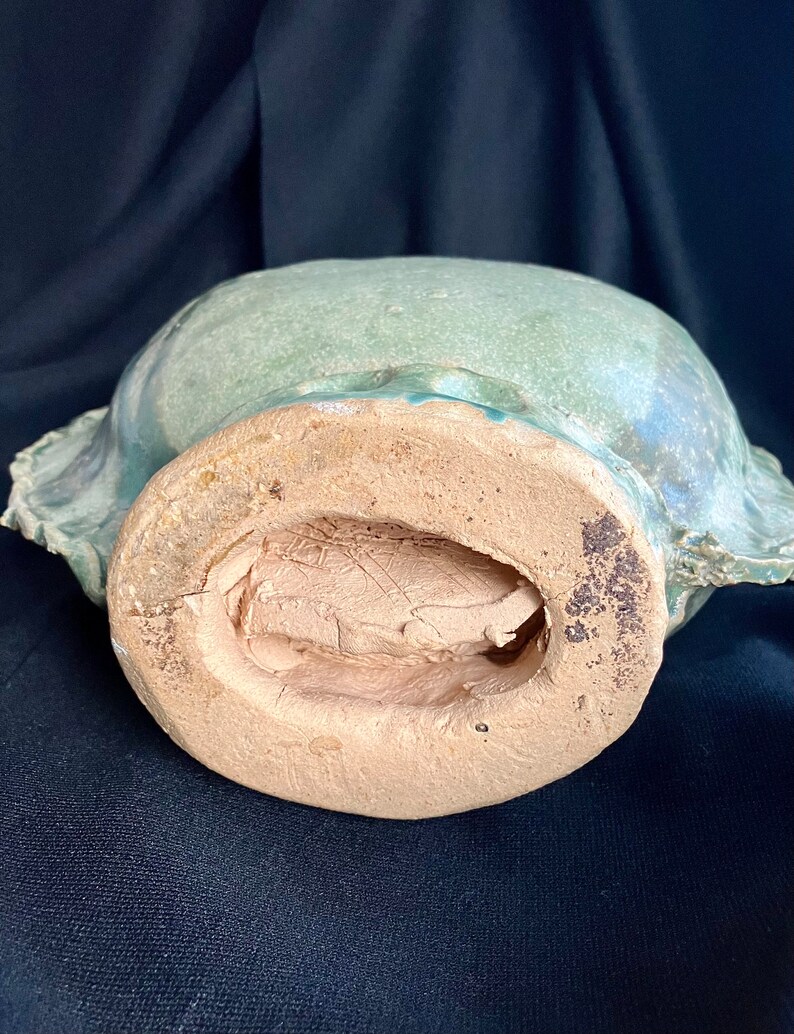K&ouml;nnte beinhalten: Die Unterseite einer gr&uuml;n glasierten Keramikschale mit einem braunen, unglasierten Boden. Die Schale hat eine abgerundete Form und einen leicht ausgestellten Rand.