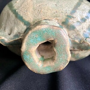 K&ouml;nnte beinhalten: Eine Keramikflasche mit gr&uuml;ner Glasur und einer strukturierten Oberfl&auml;che. Die Flasche hat einen runden K&ouml;rper und eine kleine &Ouml;ffnung oben.