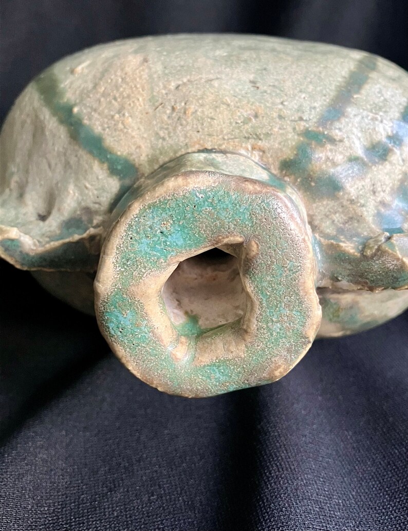 K&ouml;nnte beinhalten: Eine Keramikflasche mit gr&uuml;ner Glasur und einer strukturierten Oberfl&auml;che. Die Flasche hat einen runden K&ouml;rper und eine kleine &Ouml;ffnung oben.