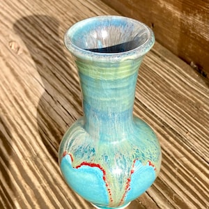 Könnte beinhalten: Eine kleine, blaue und grüne Keramikvase mit roten Akzenten. Die Vase hat einen runden Körper und einen schmalen Hals.