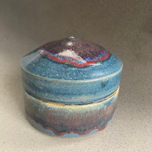 Könnte beinhalten: Eine blaue Keramikdose mit Deckel und texturierter Glasur. Der Deckel hat eine spitze Oberseite und die Dose einen abgerundeten Boden.
