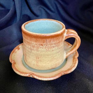 Könnte beinhalten: Ein handgemachtes Keramik-Teetassen- und Untertassen-Set in einem hellbraunen und gelben Glazure mit blauem Innenraum.