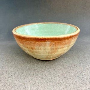 May include: A small, ceramic bowl with a light green interior and a brown, speckled exterior.