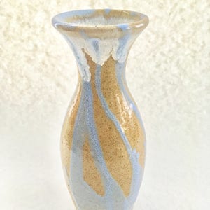 Op de afbeelding: Een kleine, lichtbruine keramische vaas met een lichtblauwe en witte glazuur. De vaas heeft een smalle hals en een rond lichaam.