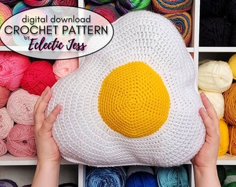 Könnte beinhalten: Ein Häkelmuster für ein weißes und gelbes Kissen in Eierform. Das Muster heißt "Eclectic Jess" und ist als digitaler Download erhältlich.