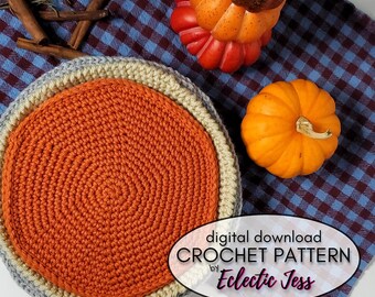 May include: A crochet pumpkin pie pattern with a gray, beige, and orange color scheme. The pattern is on a blue and white checkered fabric with two decorative pumpkins. The text on the image reads "digital download CROCHET PATTERN by Eclectic Jess".