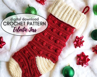 Puede incluir: Una media de Navidad de crochet roja y crema con un patrón de punto de pompón. La media tiene un puño crema y un lazo en la parte superior. La media está rodeada de adornos y lazos rojos y verdes.