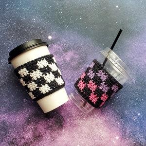 May include: Two crocheted coffee cup cozies. One is black and white checkered, the other is black with pink and purple stripes.