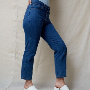 May include: A person wearing blue jeans and a light blue cardigan with white heeled mules.