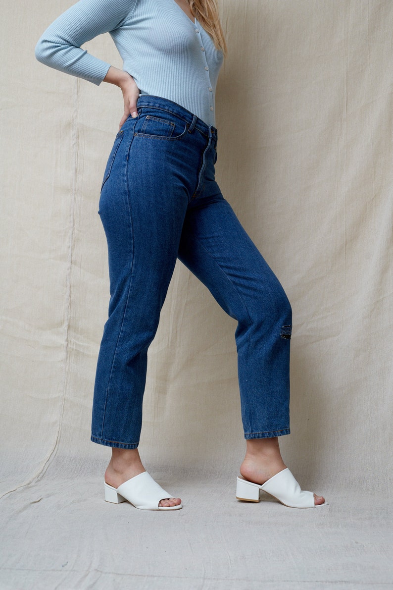 May include: A person wearing blue jeans and a light blue cardigan with white heeled mules.