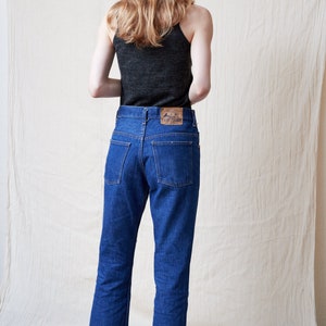 May include: A person wearing a dark gray tank top and blue denim jeans with a brown leather patch on the back pocket.