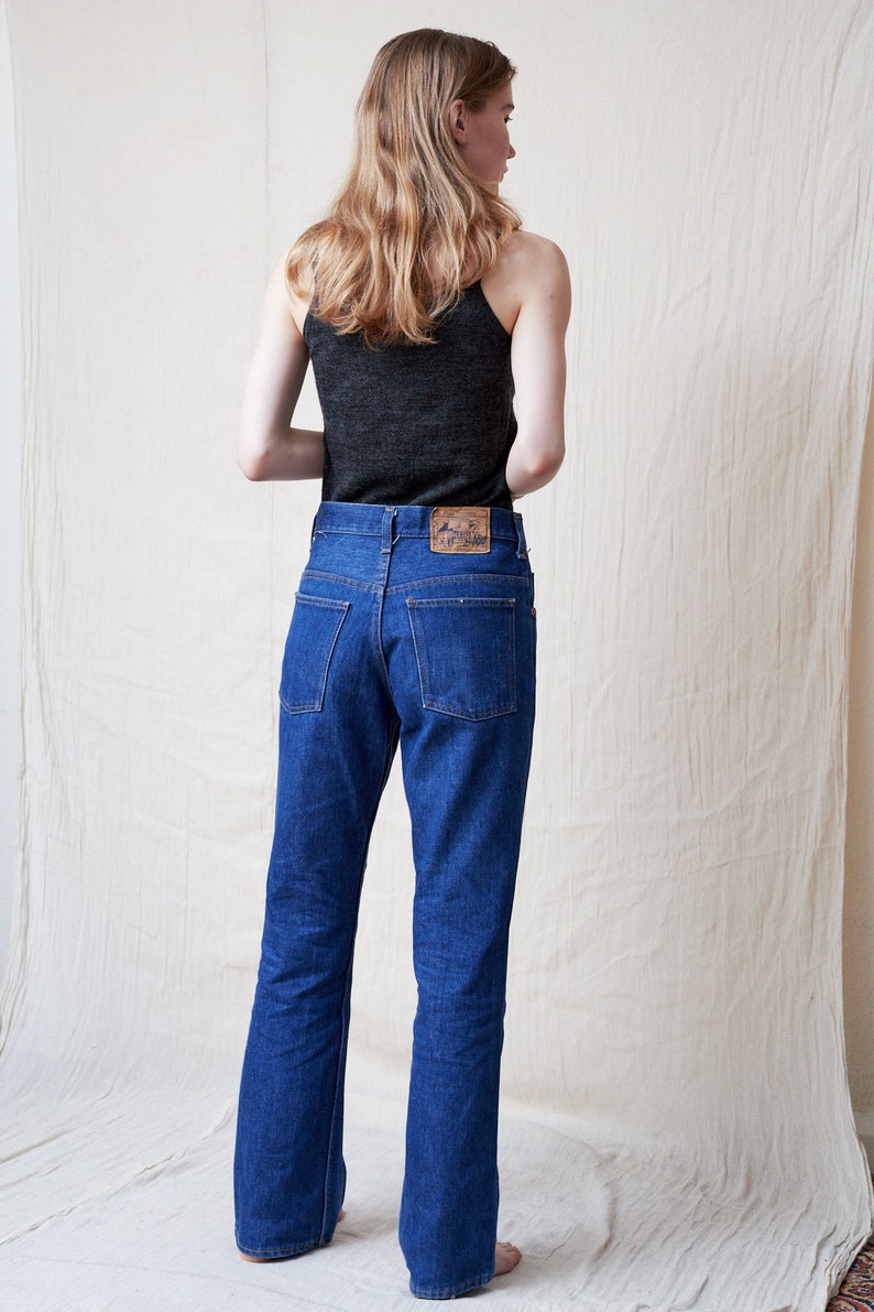 May include: A person wearing a dark gray tank top and blue denim jeans with a brown leather patch on the back pocket.